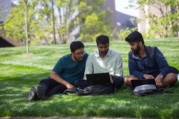 three people looking at a computer outside on campus
