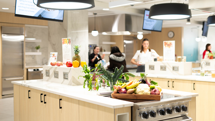 vegetables and fruits in the foreground on a countertop with the learning kitchen and two people talking in the background